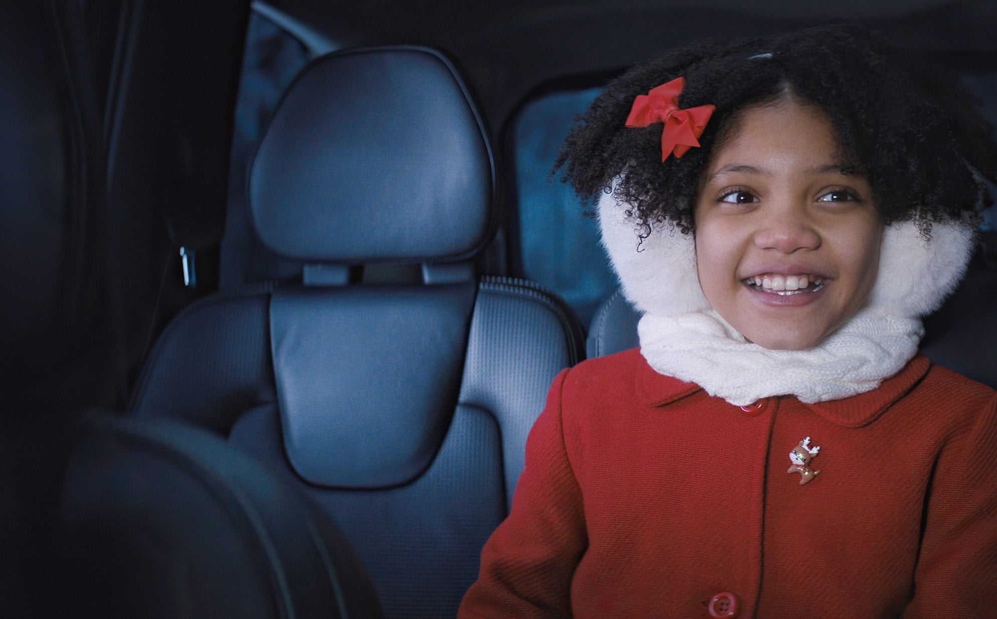 Leah Brady in a car wearing a white scarf and red coat with a flower pin, smiling