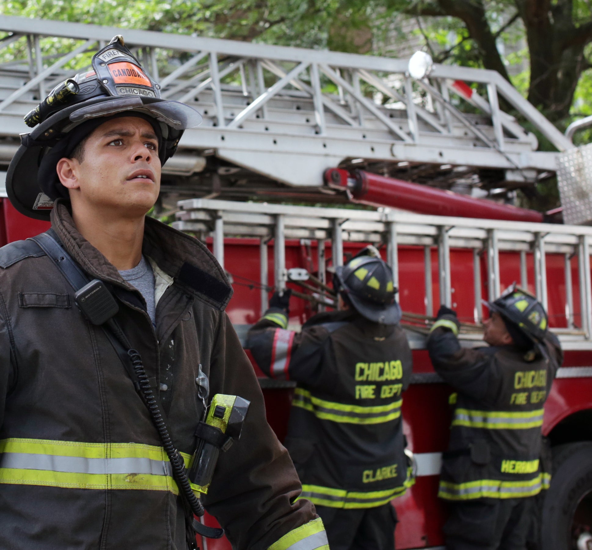 Charlie Barnett dressed in firefighter gear in front of a firetruck and other firefighters getting set up