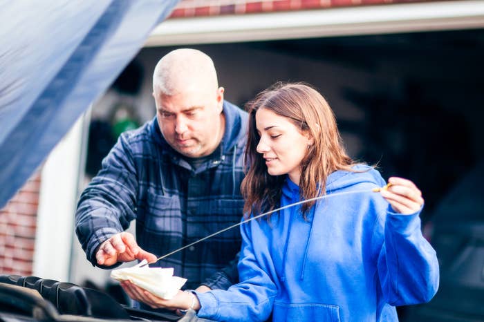 A man and a woman in casual clothing are checking the oil dipstick of a car together in a garage