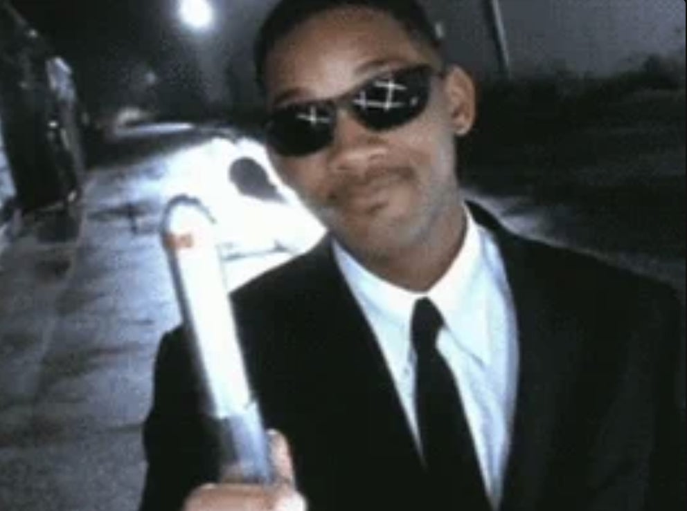 Will Smith, wearing a suit and sunglasses, points a neuralyzer, a memory-erasing device, from the film <em>Men in Black</em>