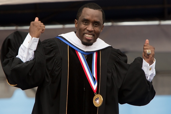 Sean "Diddy" Combs is wearing academic regalia and a medal, smiling and raising both fists in the air