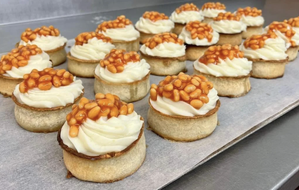 Mini tarts topped with white cream and baked beans, arranged on a baking tray