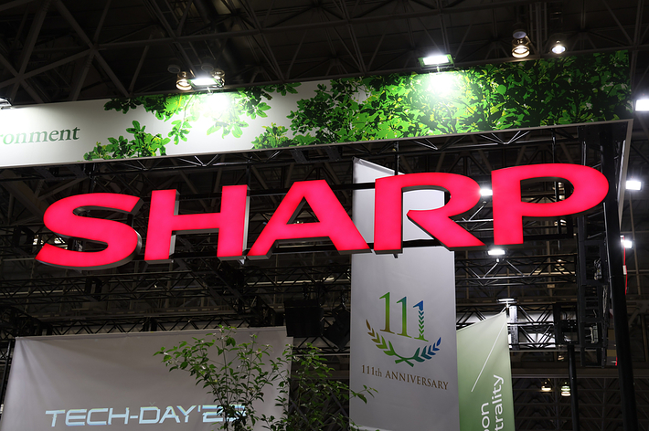 SHARPのロゴと「11th Anniversary」の看板が映っている展示ブース。背景には葉のデザインが見える。