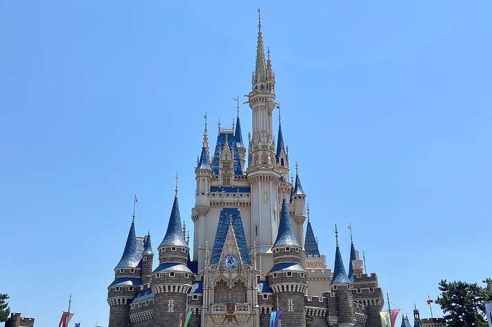 ディズニーランドのシンデレラ城が中央にそびえ立ち、多くの観光客がその前で観光を楽しんでいる。