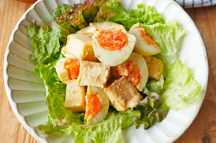 お皿に盛り付けられた、葉物野菜と卵、豆腐サラダの料理。背景にお皿と布巾が見える。