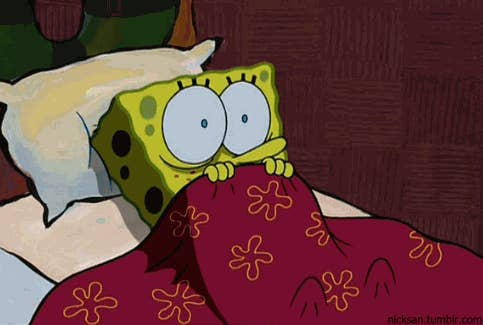 SpongeBob SquarePants lies in bed, holding a blanket up to his nose, looking scared with wide eyes