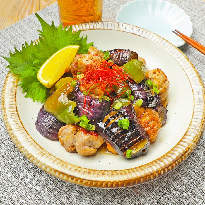 器に盛られた焼きなす、ピーマンの料理。上には輪切りねぎと糸唐辛子がトッピングされており、横にレモンが添えられています。