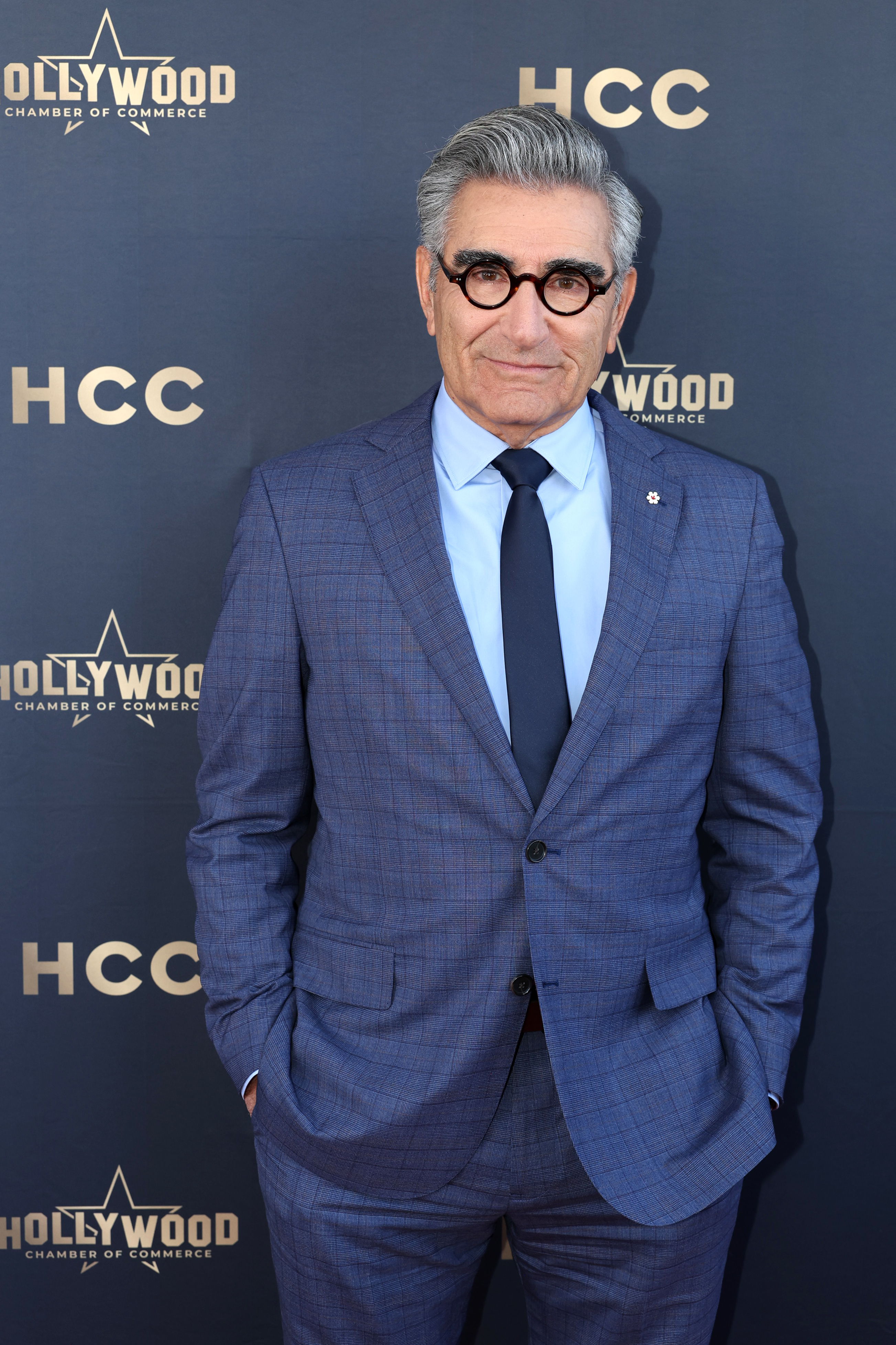 Eugene Levy on the red carpet, wearing a blue suit and tie, with round glasses at the Hollywood Chamber of Commerce event