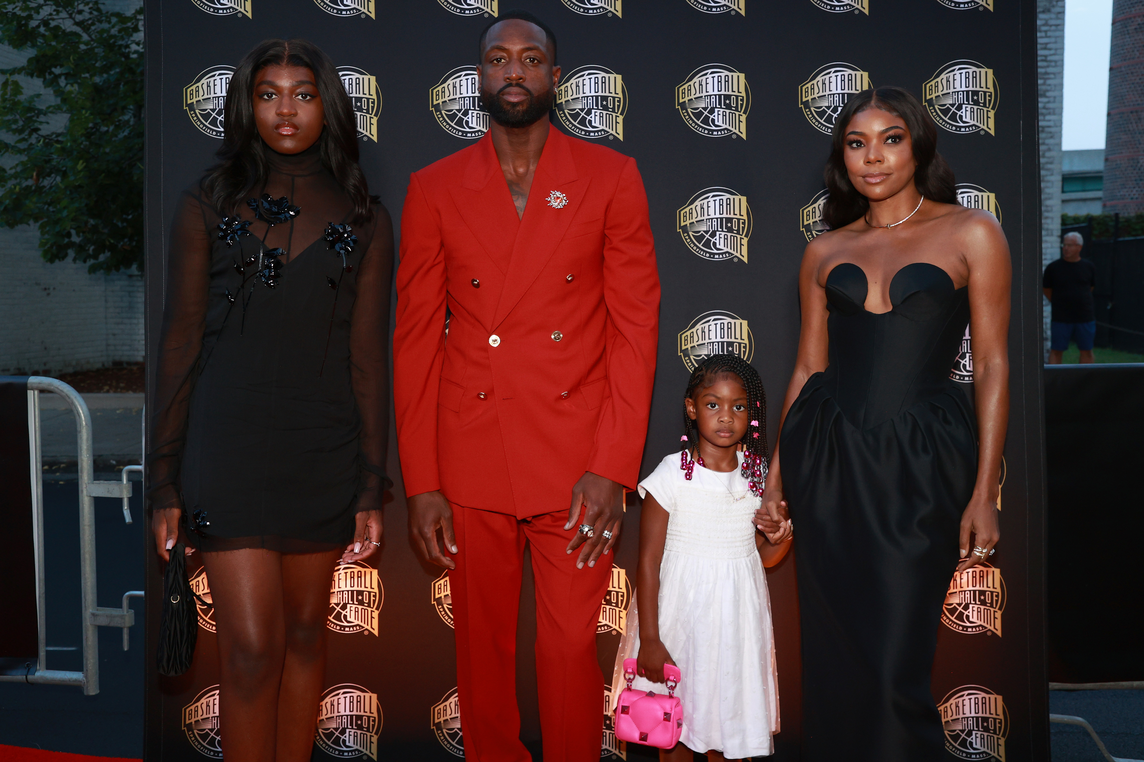 Zaya Wade, Dwyane Wade, Kaavia James, and Gabrielle Union pose on the red carpet. Dwyane wears a red suit, Zaya a black dress, Kaavia a white dress, and Gabrielle a black gown