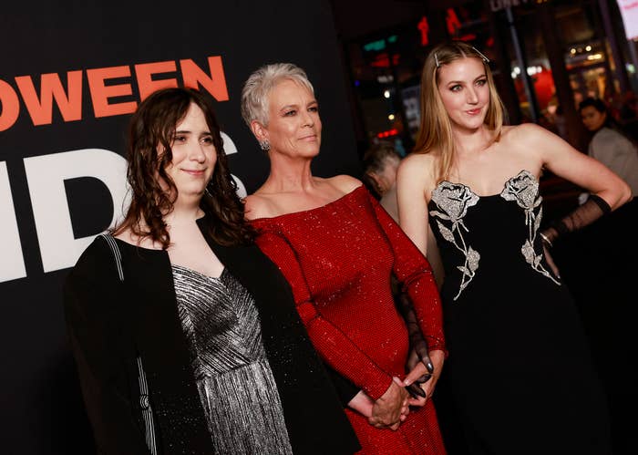 Ruby Guest, Jamie Lee Curtis, and Annie Guest pose on the red carpet. Ruby wears a silver dress, Jamie wears a red dress, and Annie wears a black dress with floral designs