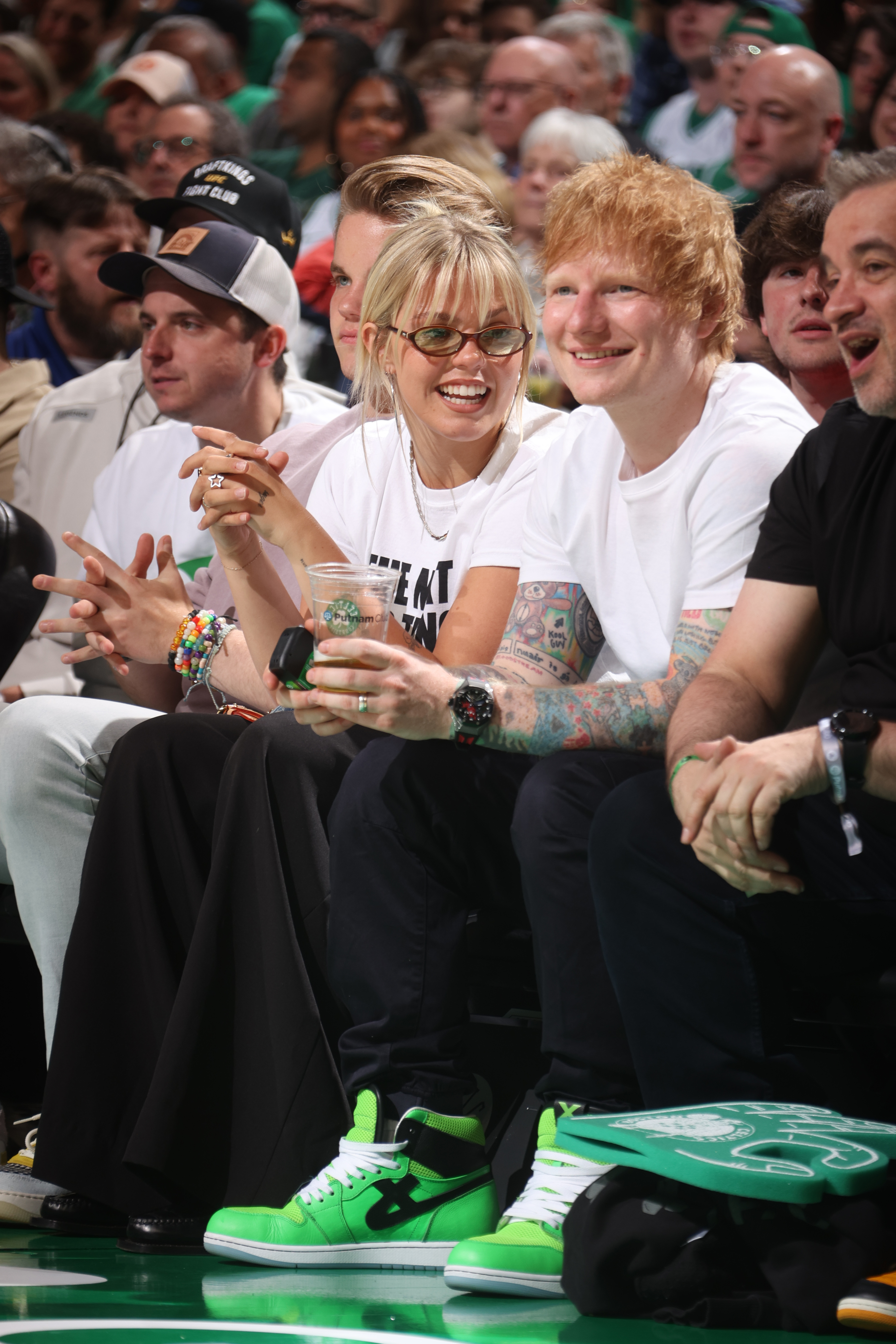 Ed Sheeran and Reneé Rapp sitting courtside at a basketball game, smiling