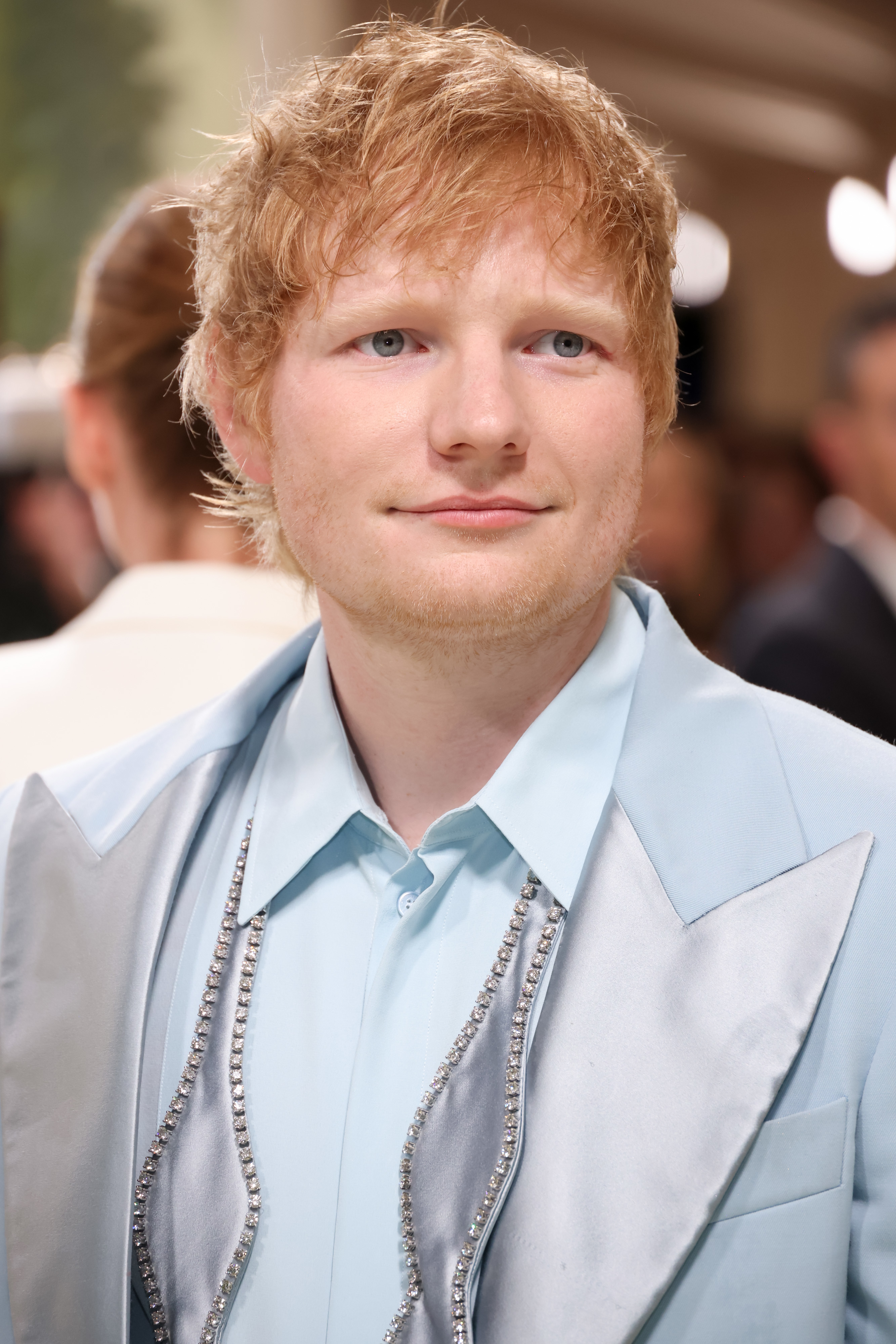 Ed Sheeran at an event, wearing a light shirt and a matching silk suit jacket with rhinestone detailing