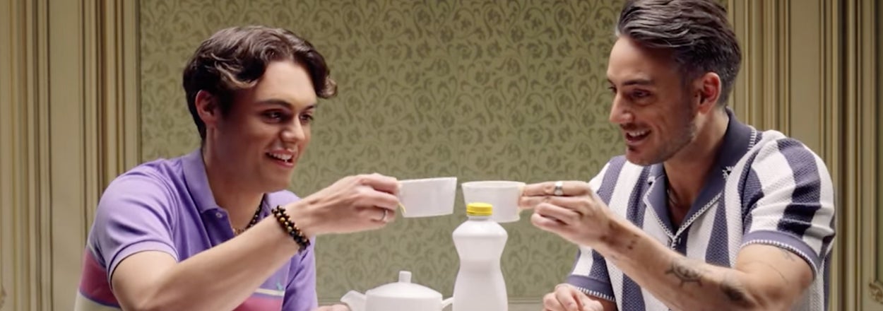 Two individuals in casual attire share a toast with small cups at a table set with snacks and beverages