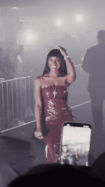 Normani, wearing a strapless, fitted leather dress, holds a microphone and dances