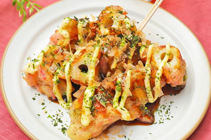 タコ焼きの盛り付け。串が刺さっていて、ソースとマヨネーズがかかっています。背景に飲み物のグラスが見えます。