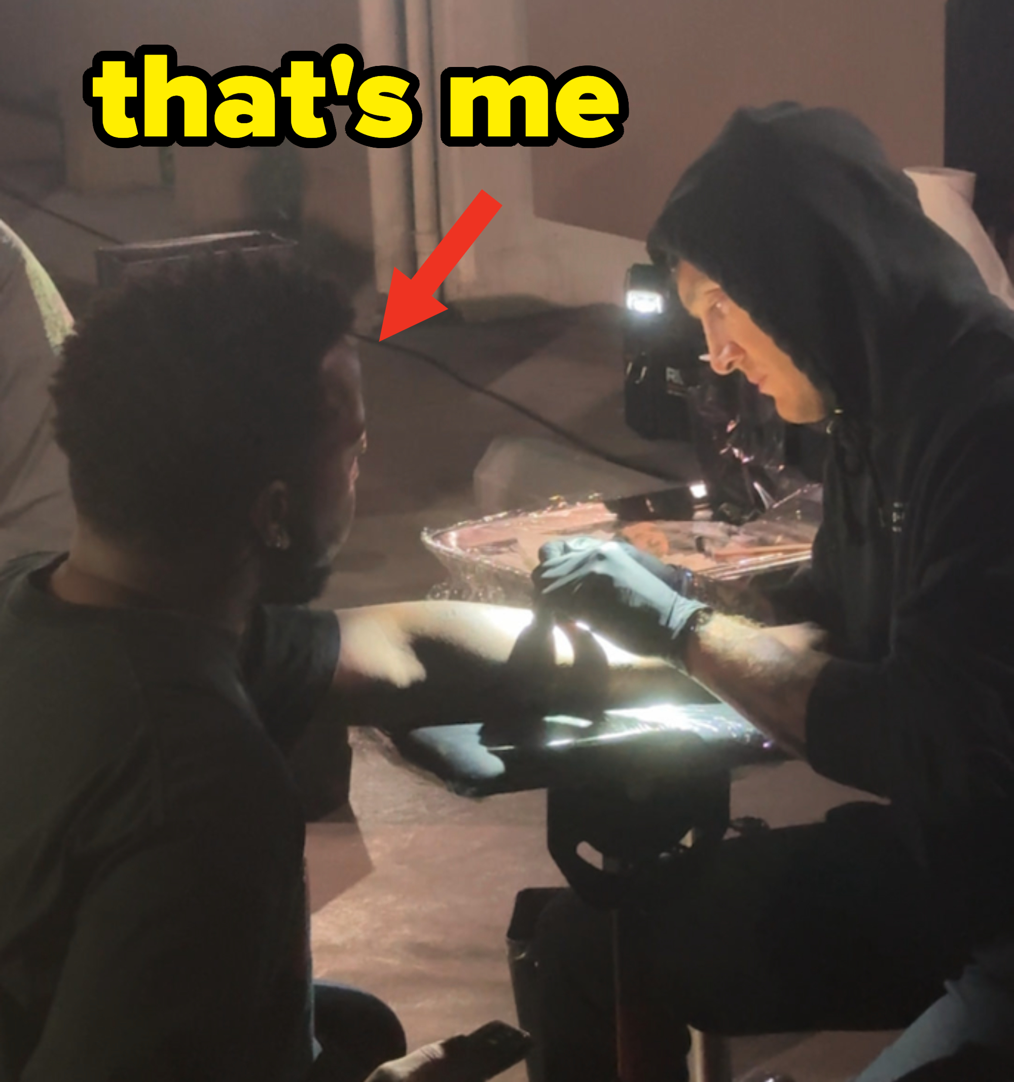 Close-up of two people; one is getting a tattoo on their forearm from a tattoo artist dressed in a hoodie and gloves