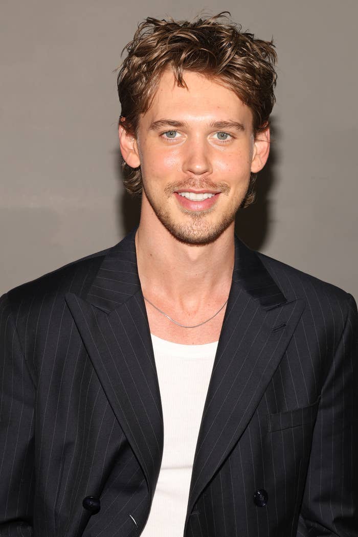 Austin Butler wearing a pinstripe blazer and a white shirt, smiling at the camera during a photoshoot