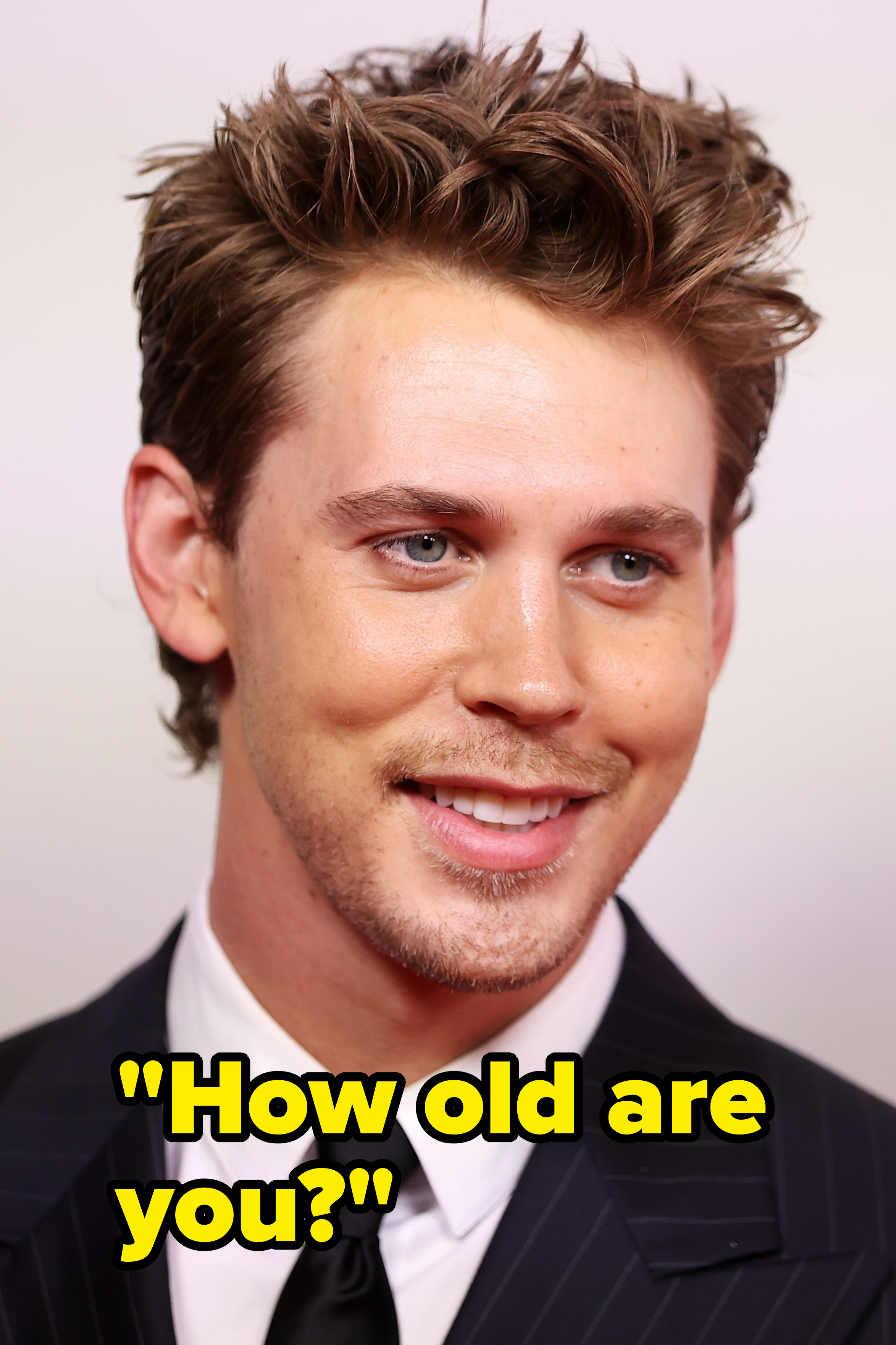 Austin Butler smiles, wearing a dark suit, white shirt, and tie at a celebrity event