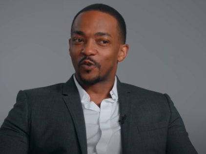 Anthony Mackie is pictured wearing a suit and open-collared shirt, sitting and looking off-camera