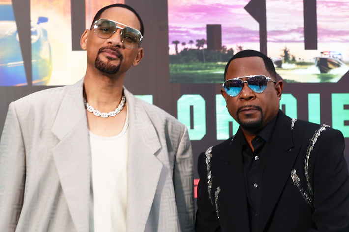 Will Smith and Martin Lawrence at the red carpet premiere, both wearing sunglasses and stylish suits, standing in front of a movie poster backdrop