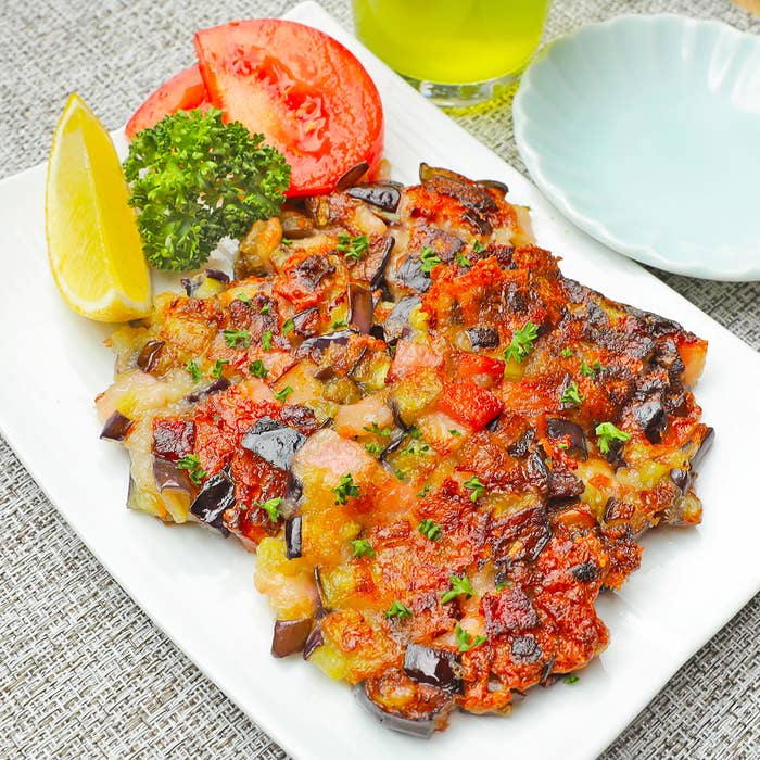 おいしそうなナスのグリルとトマト、レモンスライス、パセリの盛り合わせが白い皿に乗っている食事。