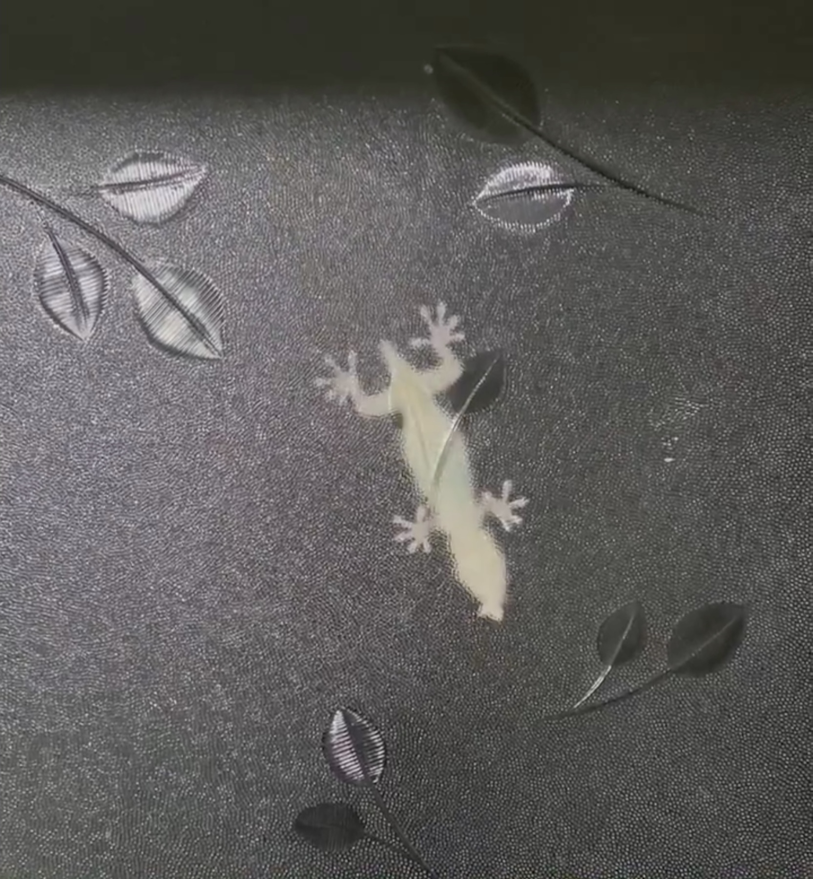 ヤモリが葉っぱのデザインが施された壁に張り付いている様子。