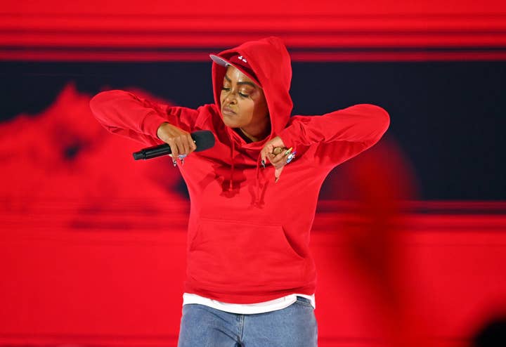 A person in a red hoodie and cap passionately performs on stage holding a microphone