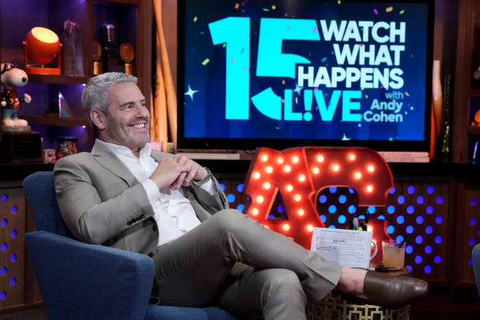 Andy Cohen is sitting on a talk show set of "Watch What Happens Live" celebrating its 15th anniversary