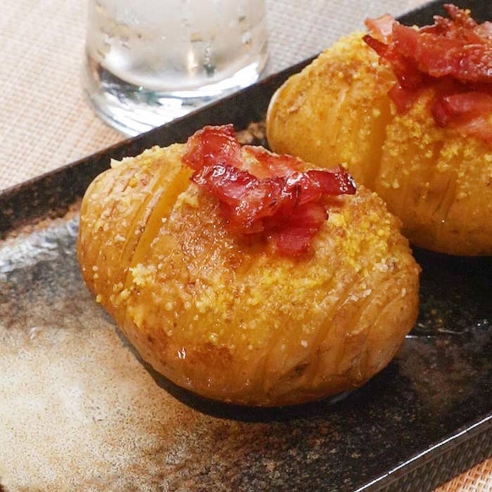 2つのベイクドポテトにベーコンのトッピングが載っている料理。背景にはグラスが写っています。