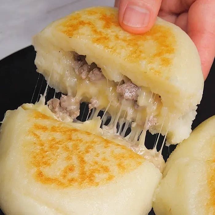 手がチーズと肉が詰まった焼いたパンを持ち上げている様子。