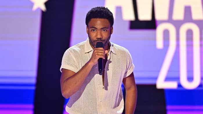 Donald Glover wearing a casual shirt, holding a microphone on stage at a music awards event