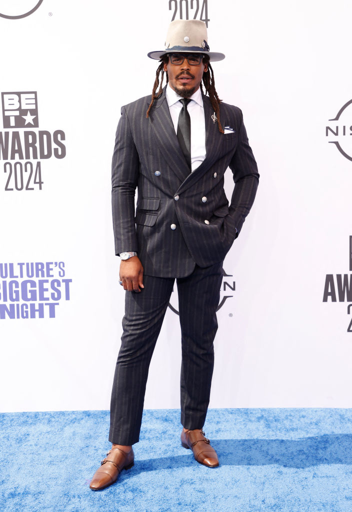 Cam Newton in a pinstripe suit, white shirt, black tie, hat, glasses, brown shoes, at the BET Awards 2024