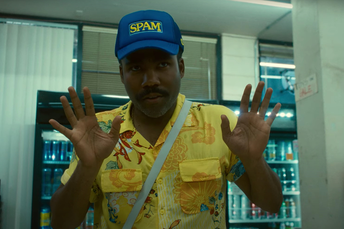 Man wearing a "Spam" hat and yellow floral shirt with white shoulder bag gestures with both hands in a store