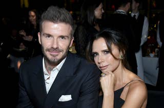 David Beckham and Victoria Beckham seated at an event, with Victoria wearing a sleeveless black dress and David in a black suit