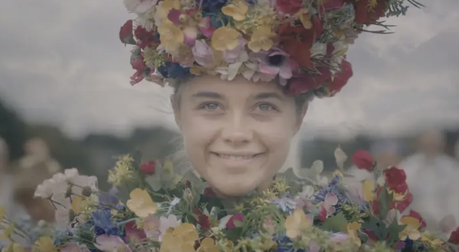 Florence Pugh, smiling, wears a large, elaborate floral headpiece and matching floral garland in an outdoor setting