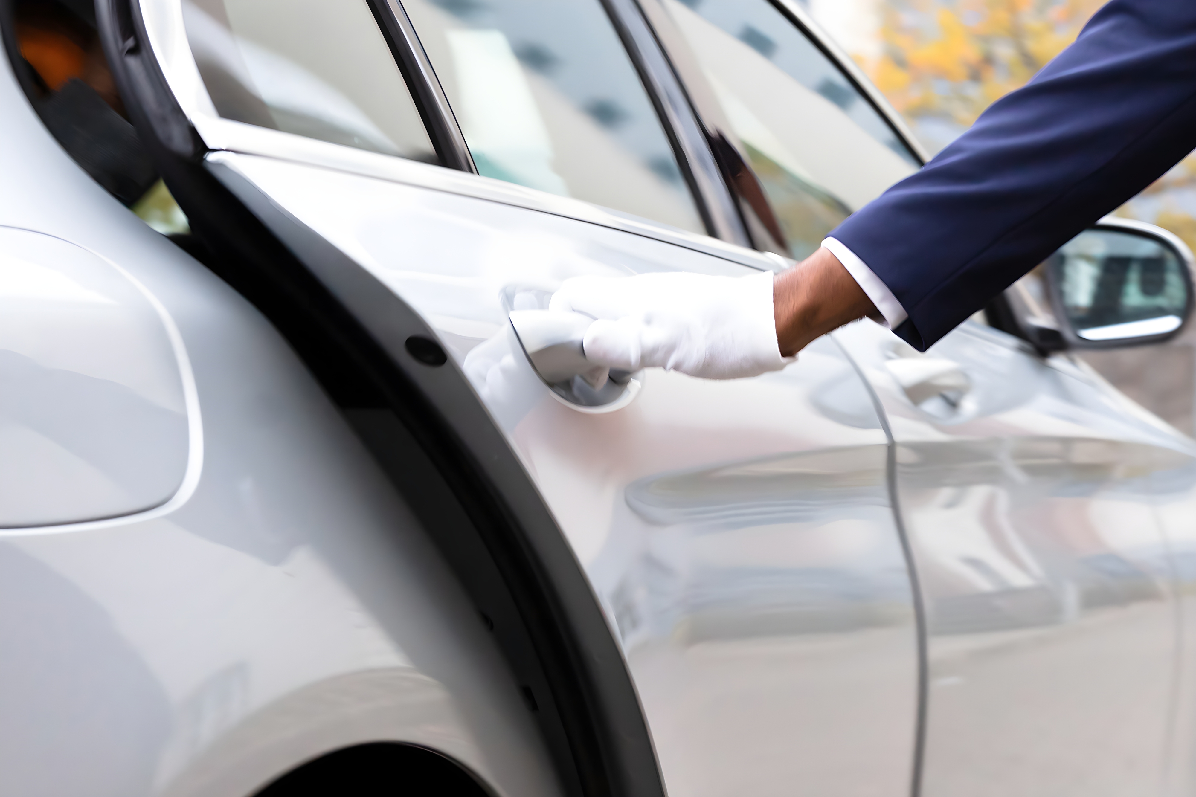 Close-up of a white-gloved hand holding a car door handle, suggesting a chauffeur or luxury service