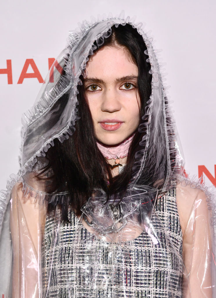 Grimes wears a translucent, frilly hooded dress with a tweed underlayer at a Chanel event