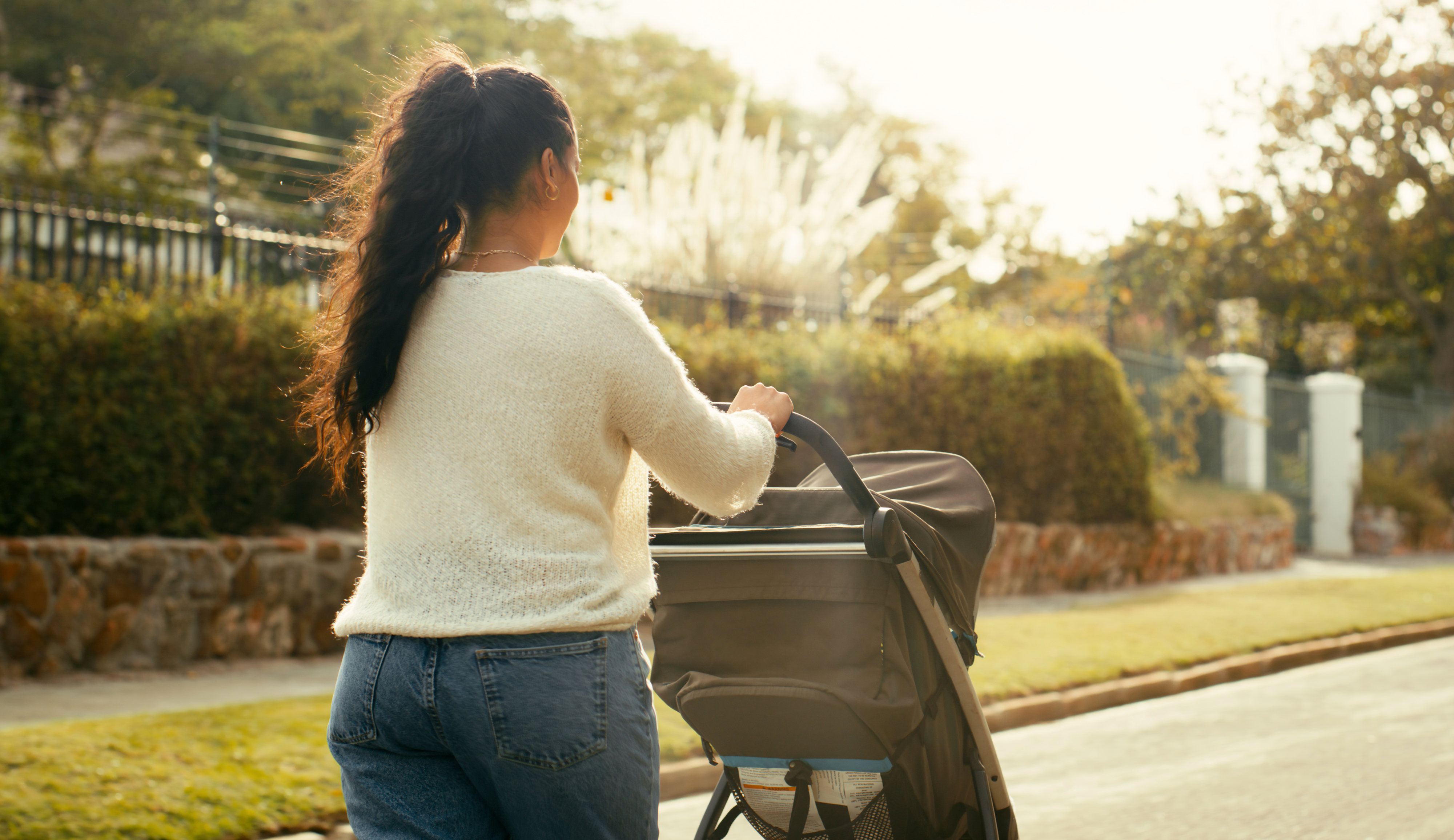 A person is seen pushing a baby stroller along a sidewalk in a residential area, wearing casual clothing