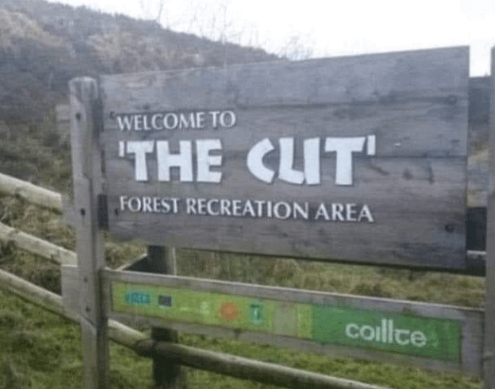 A wooden sign reading &quot;Welcome to 'The Cut' Forest Recreation Area,&quot; but the u in &quot;The cut&quot; makes it look like it says &quot;Welcome to 'The Clit'&quot;