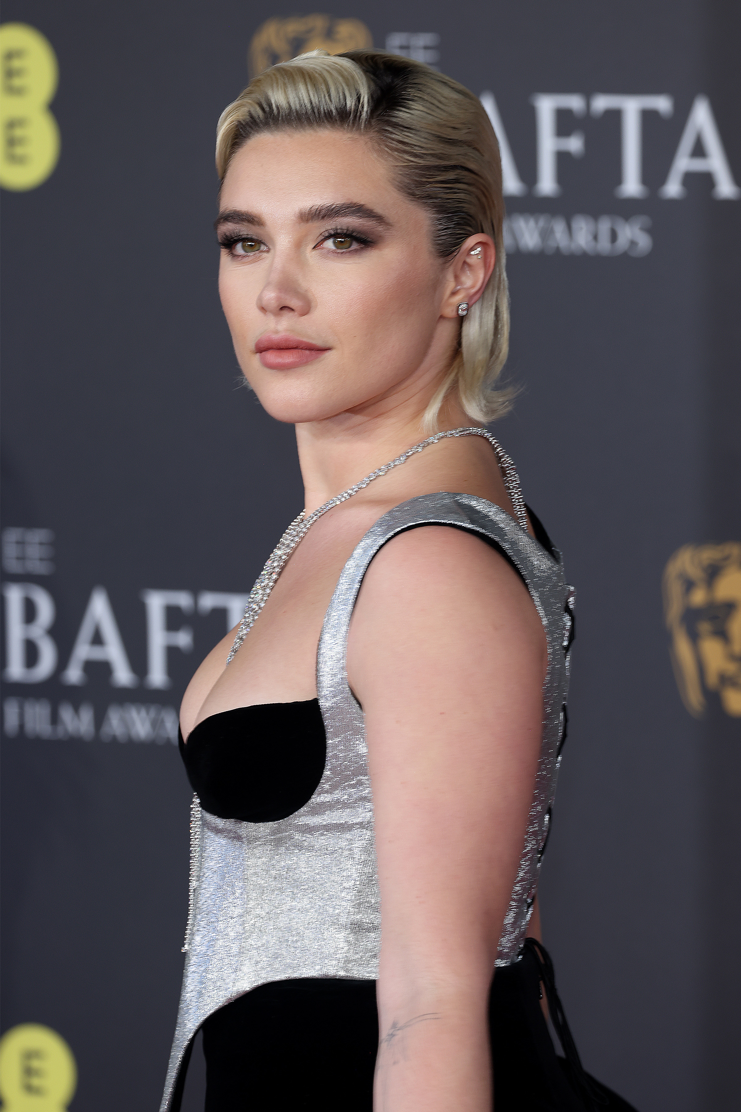 Florence Pugh on the BAFTA red carpet in a shimmering gown, featuring metallic details and a deep neckline