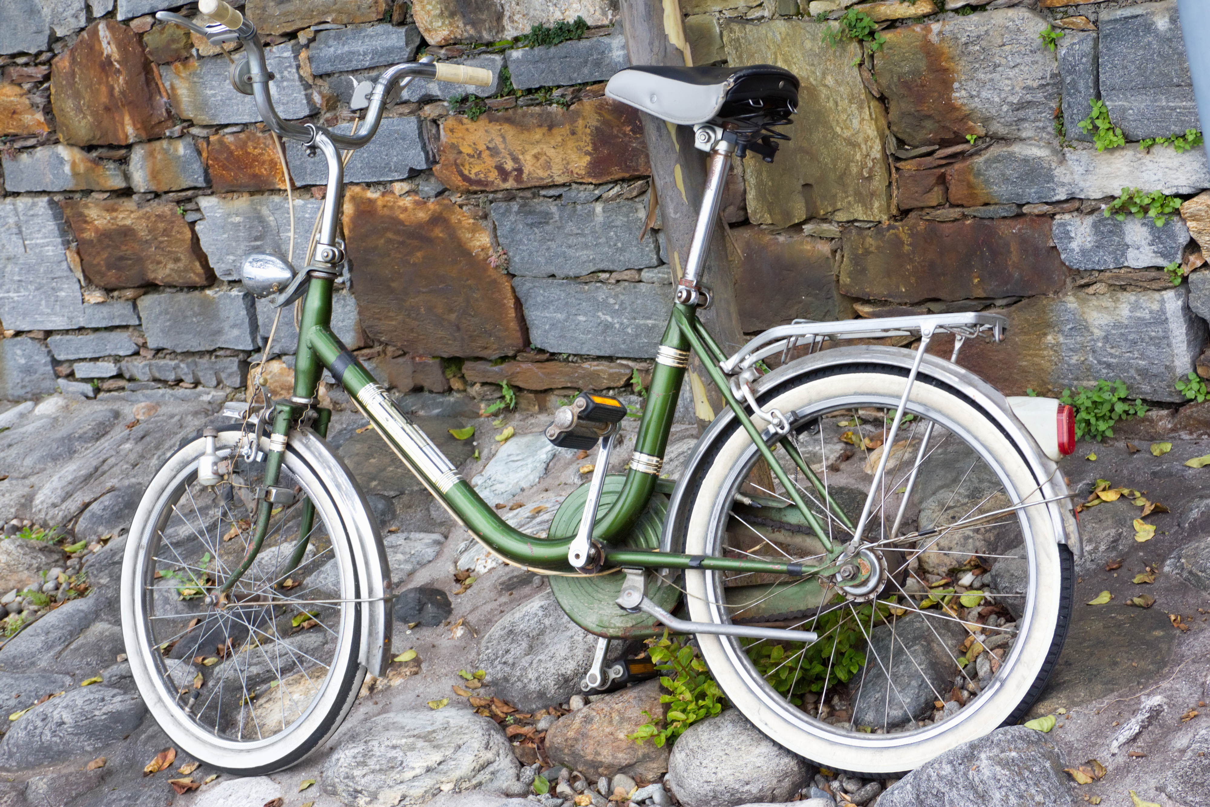 A vintage bicycle with a sturdy metal frame and white-tread tires is parked on a cobblestone street in front of a stone wall