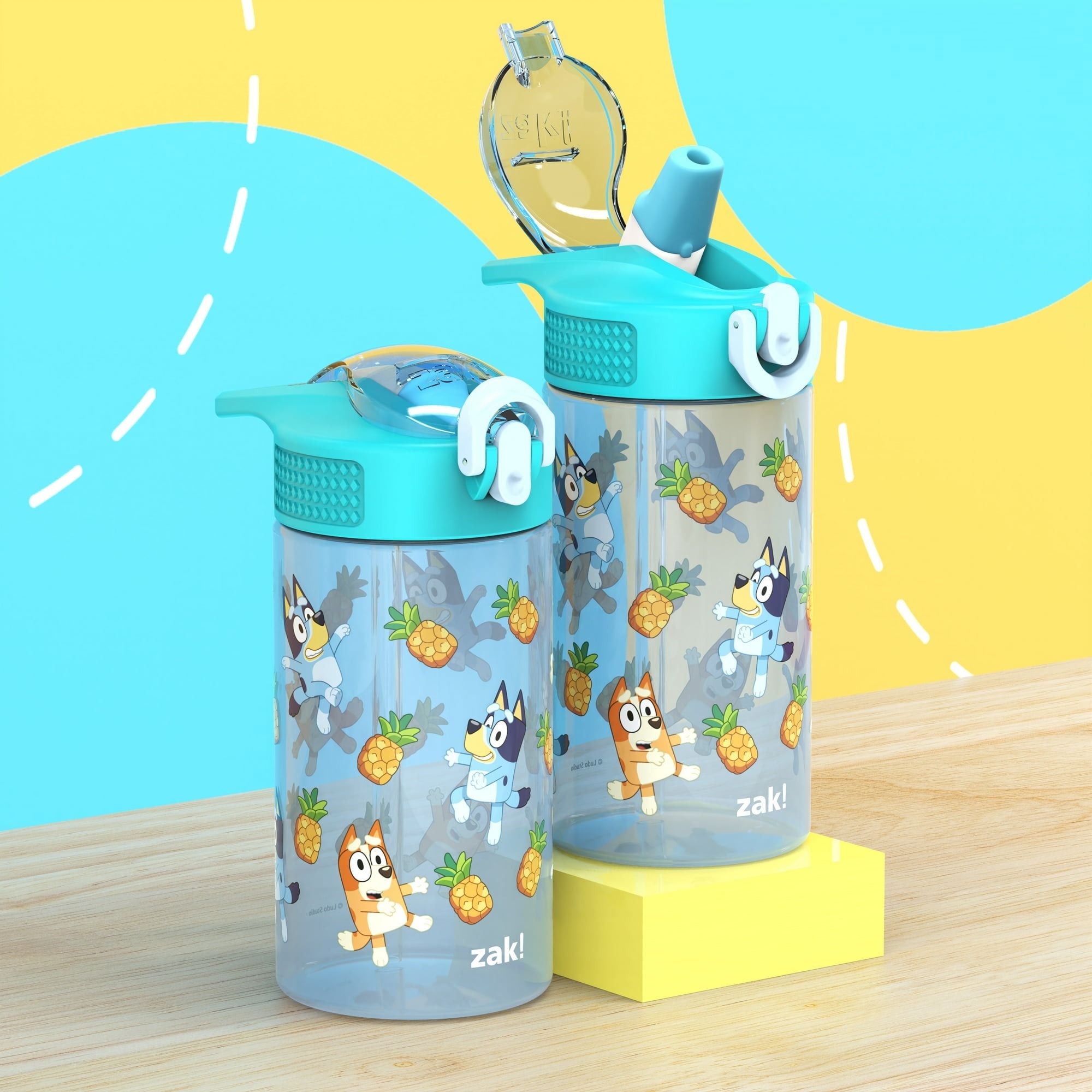 Zak water bottles featuring Bluey characters and pineapple graphics, standing on a wooden surface with a colorful background, suitable for children
