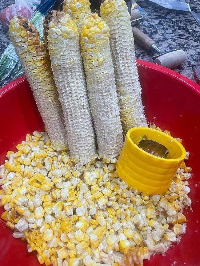 reviewer's orn cobs with kernels removed, shown in a red bowl with loose kernels and a yellow corn stripper tool