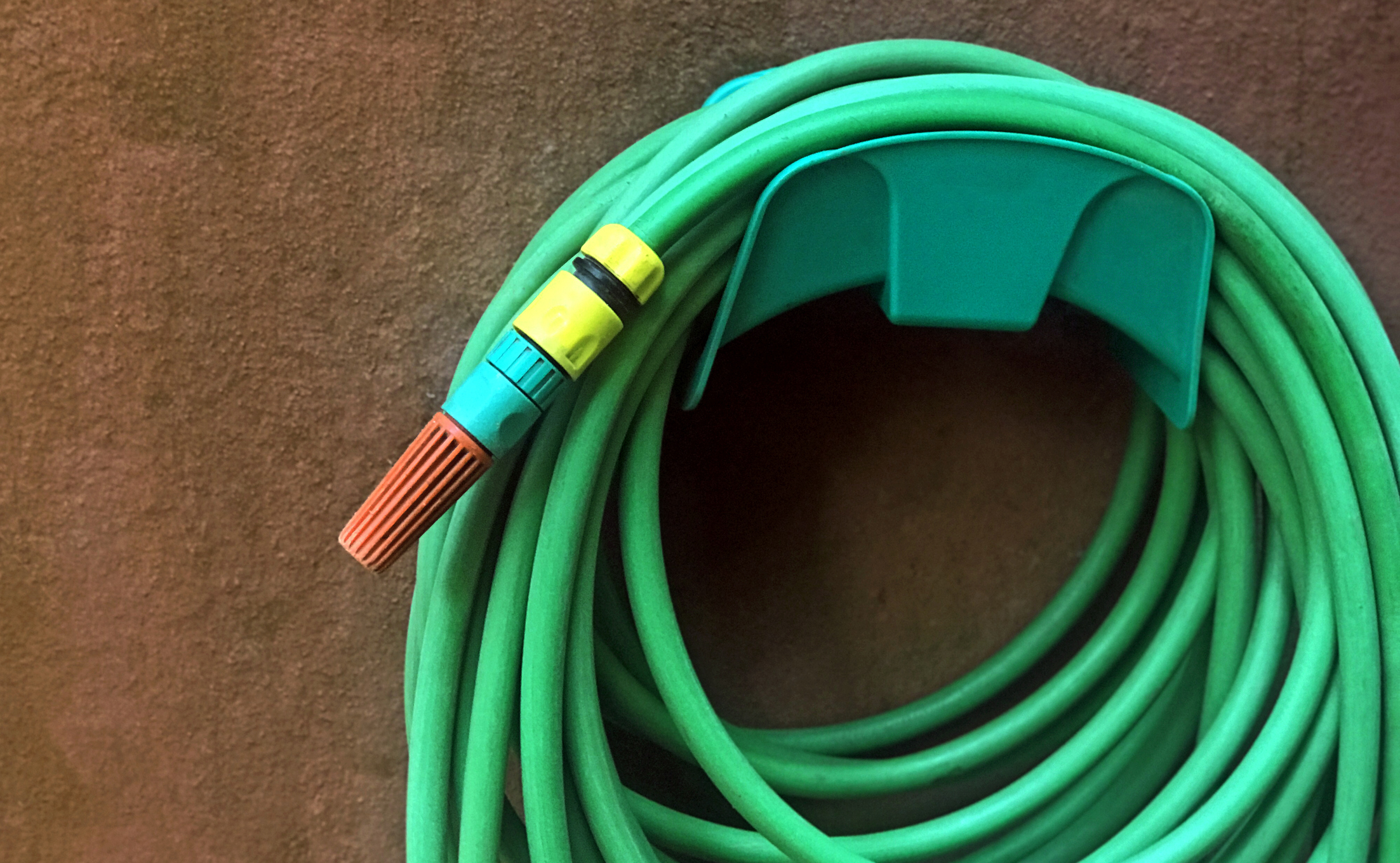 A coiled green garden hose is neatly stored with a plastic hanger. A hose nozzle is attached to the end