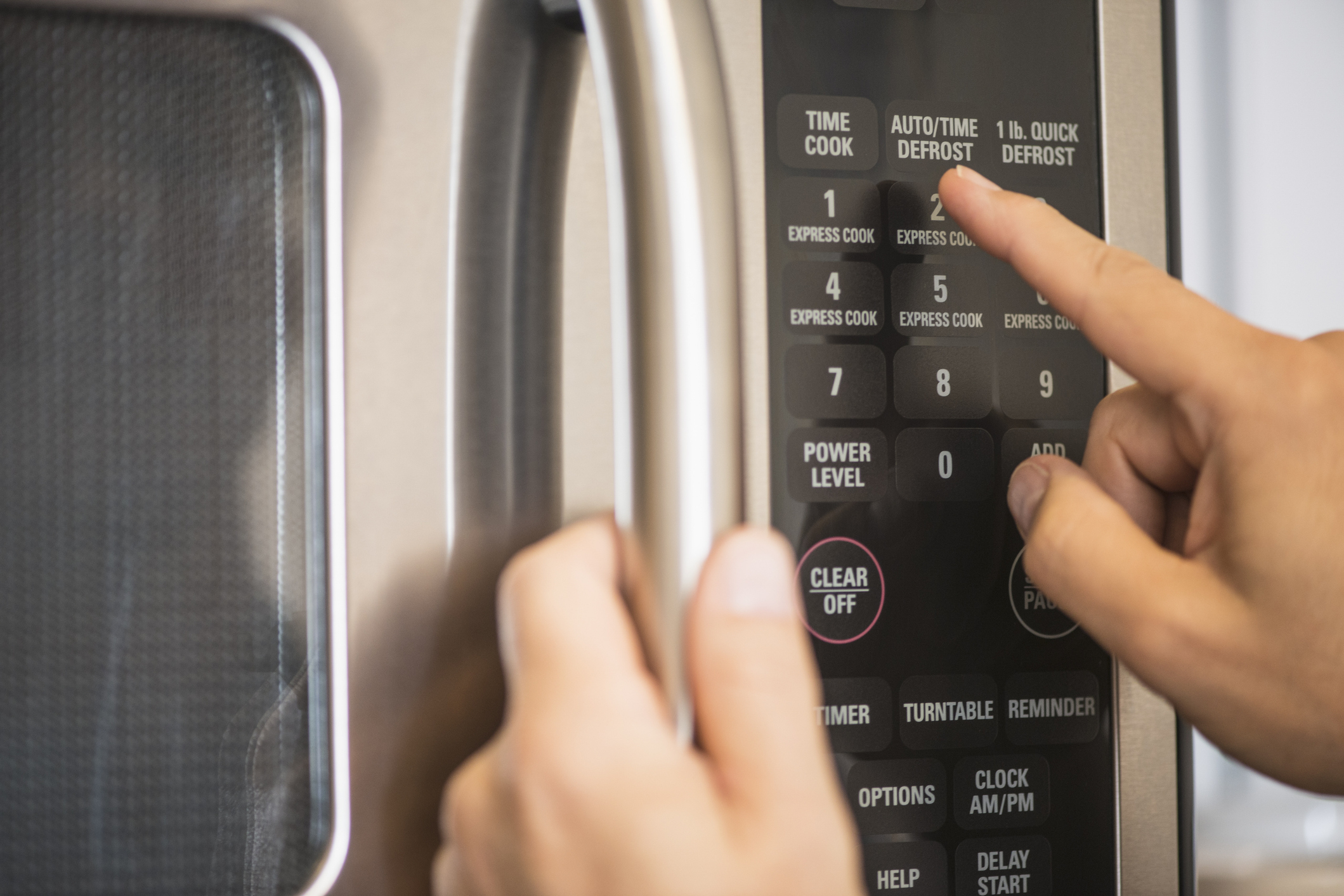 Close-up of a person's hand pressing the "1 lb. Quick Defrost" button on a microwave control panel while holding the handle