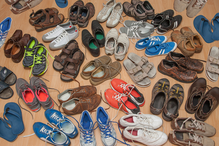 Various types of footwear, including sneakers, sandals, and dress shoes, are scattered on a wooden floor, illustrating diverse fashion styles