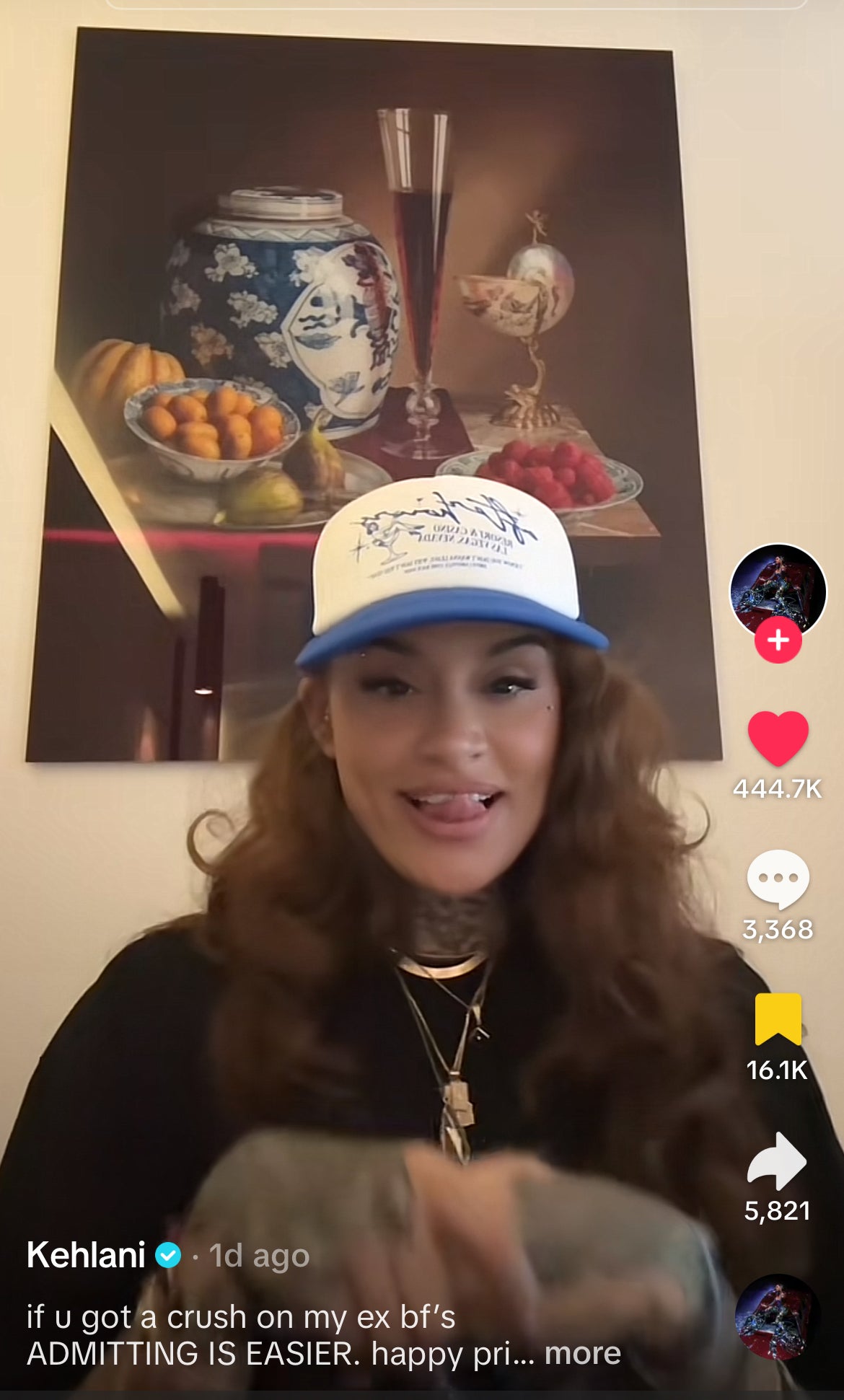 Kehlani is seen wearing a white and blue cap and casual attire, smiling in front of a still-life painting. The TikTok post caption reads: "if u got a crush on my ex bf’s ADMITTING IS EASIER. happy pri…more."