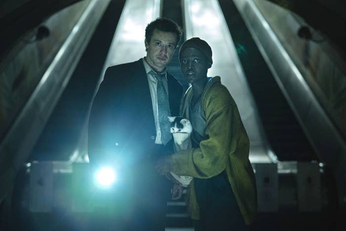 Joseph Quinn, Lupita Nyong'o, and Frodo standing in front of escalators while holding a flashlight in a scene from &quot;A Quiet Place: Day One&quot;