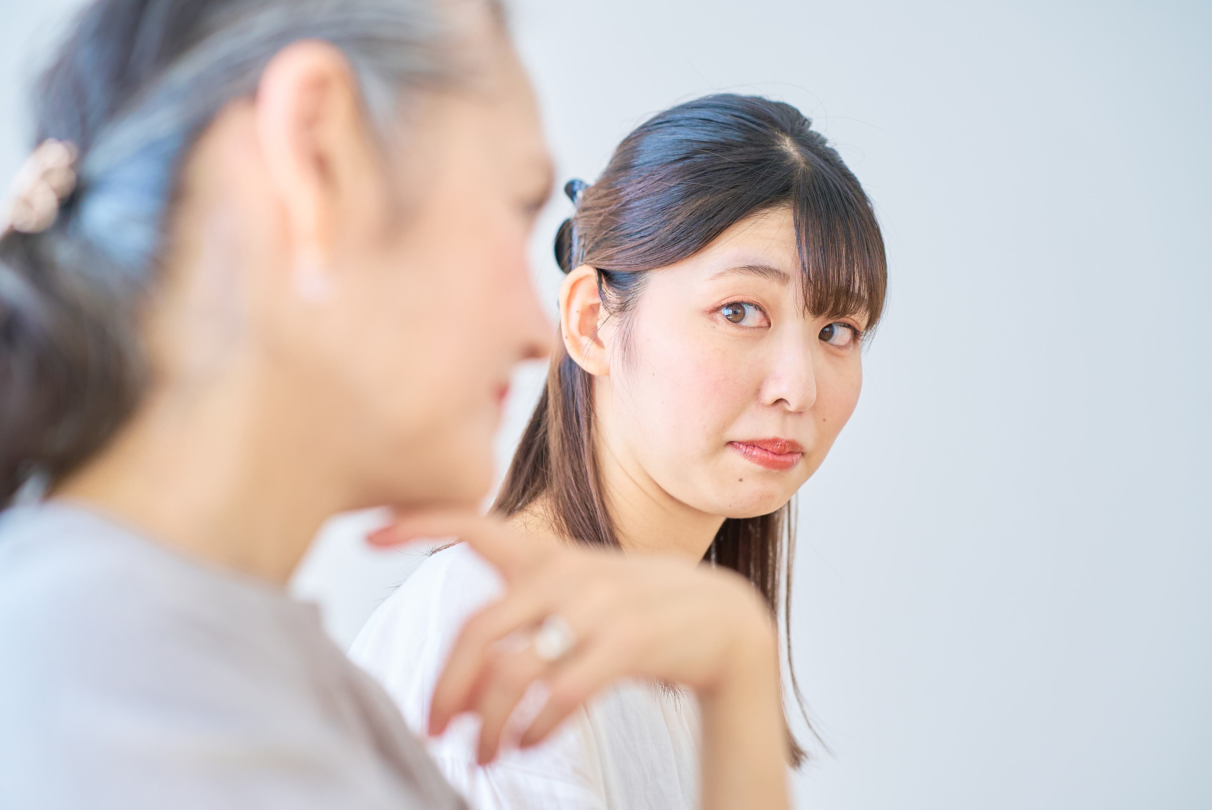 Two women engaged in conversation, one older in the foreground, and a younger woman with long hair in the background, looking to the side