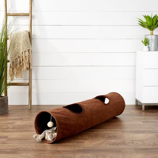 A cat peeks out from the brown cat tunnel toy with holes and a hanging ball